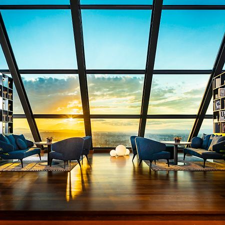 Grand Hotel Millennium โซเฟีย ภายนอก รูปภาพ The photo depicts a modern, stylish interior of a high-rise space with a panoramic view through large glass windows. The scene features a cozy seating area with several blue armchairs arranged around a low table, creating a comfortable atmosphere. Th