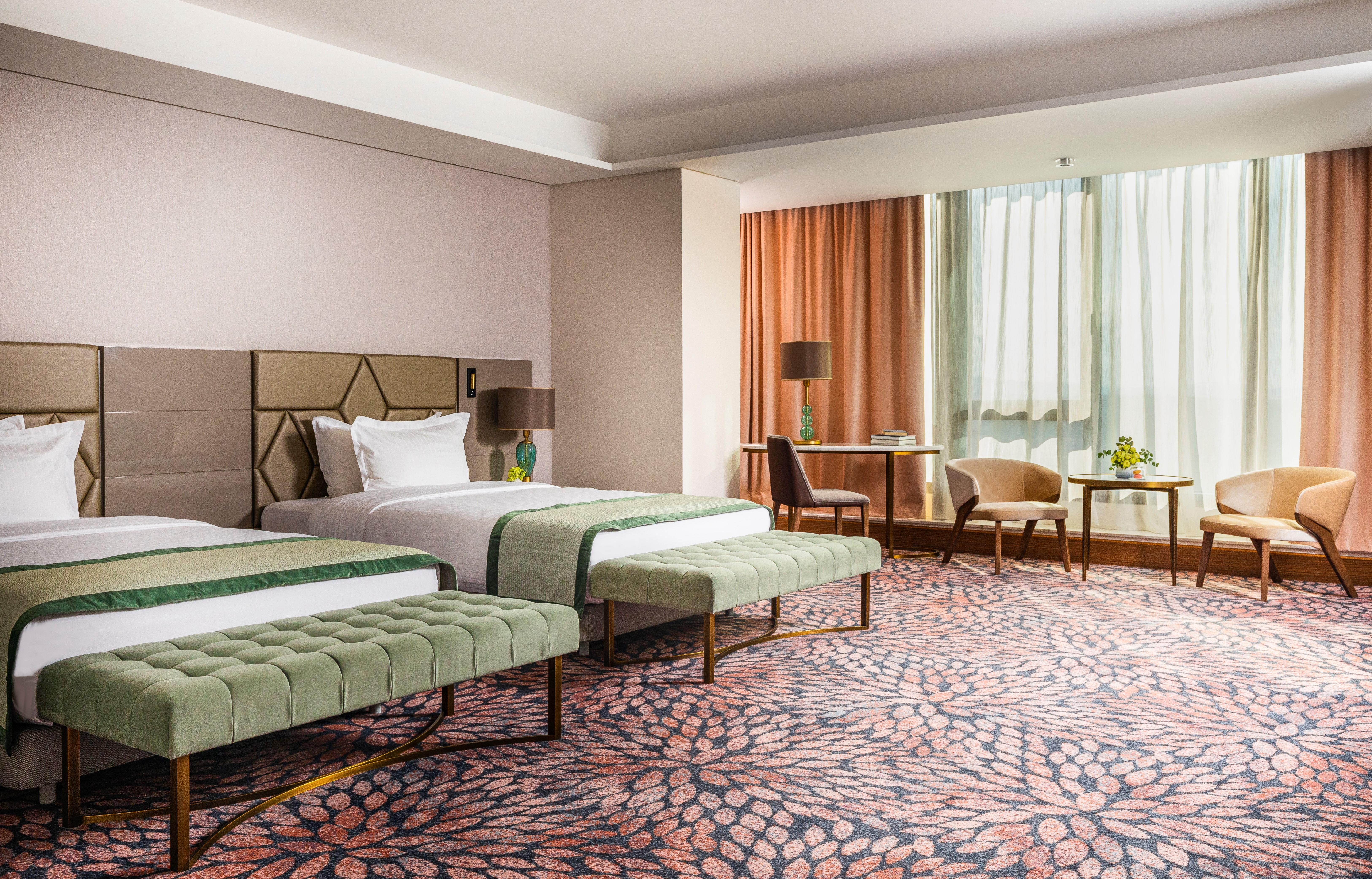 Grand Hotel Millennium โซเฟีย ภายนอก รูปภาพ The image shows a well-decorated hotel room featuring two beds with green striped bedspreads. There is a plush green bench at the foot of each bed. The room has large windows with sheer curtains allowing natural light to enter. There is a cozy seatin