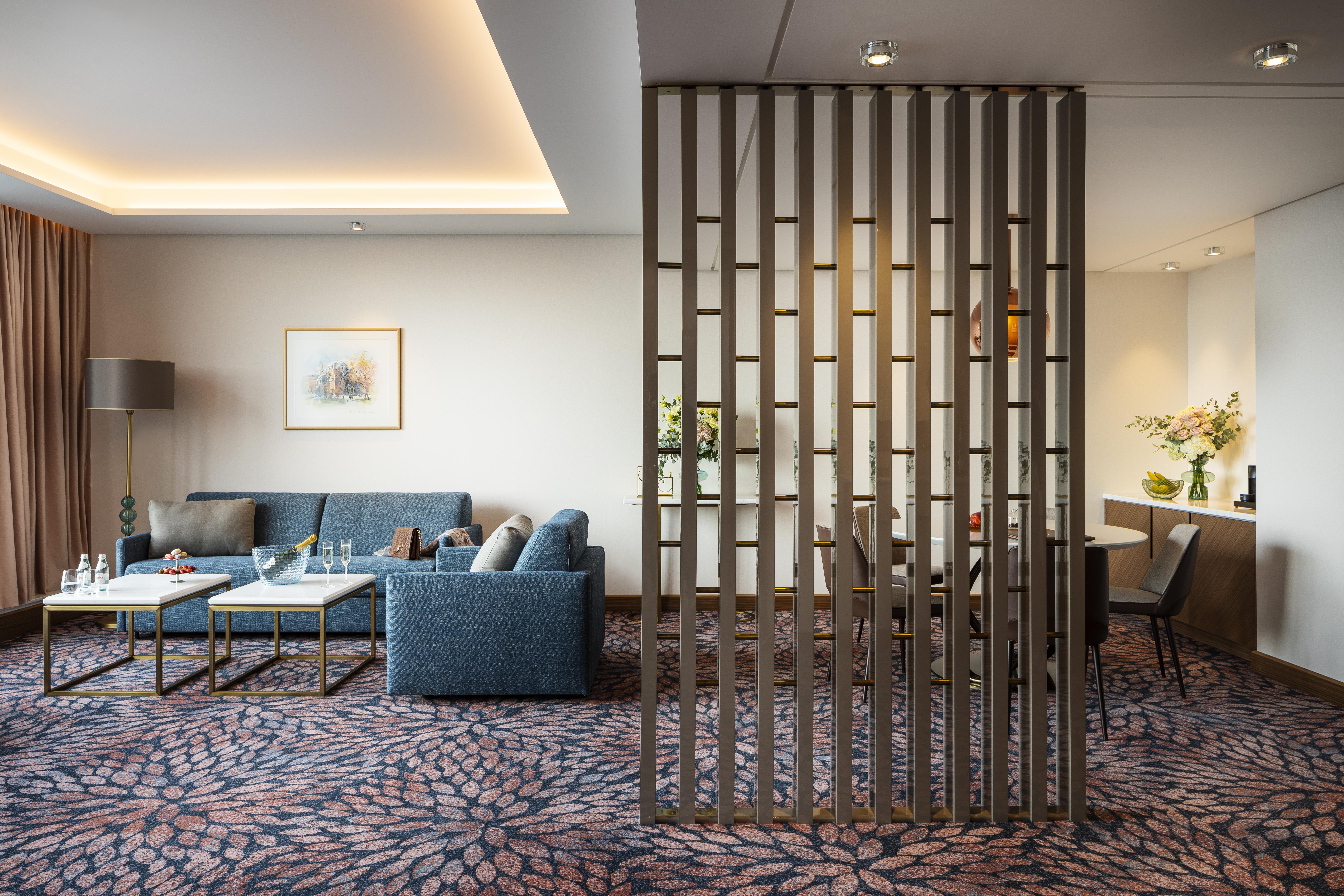 Grand Hotel Millennium โซเฟีย ภายนอก รูปภาพ The photo shows a modern living space with a comfortable seating area featuring a blue couch and two coffee tables. There is a decorative partition made of vertical wooden slats, which separates this sitting area from a dining space. The dining area 