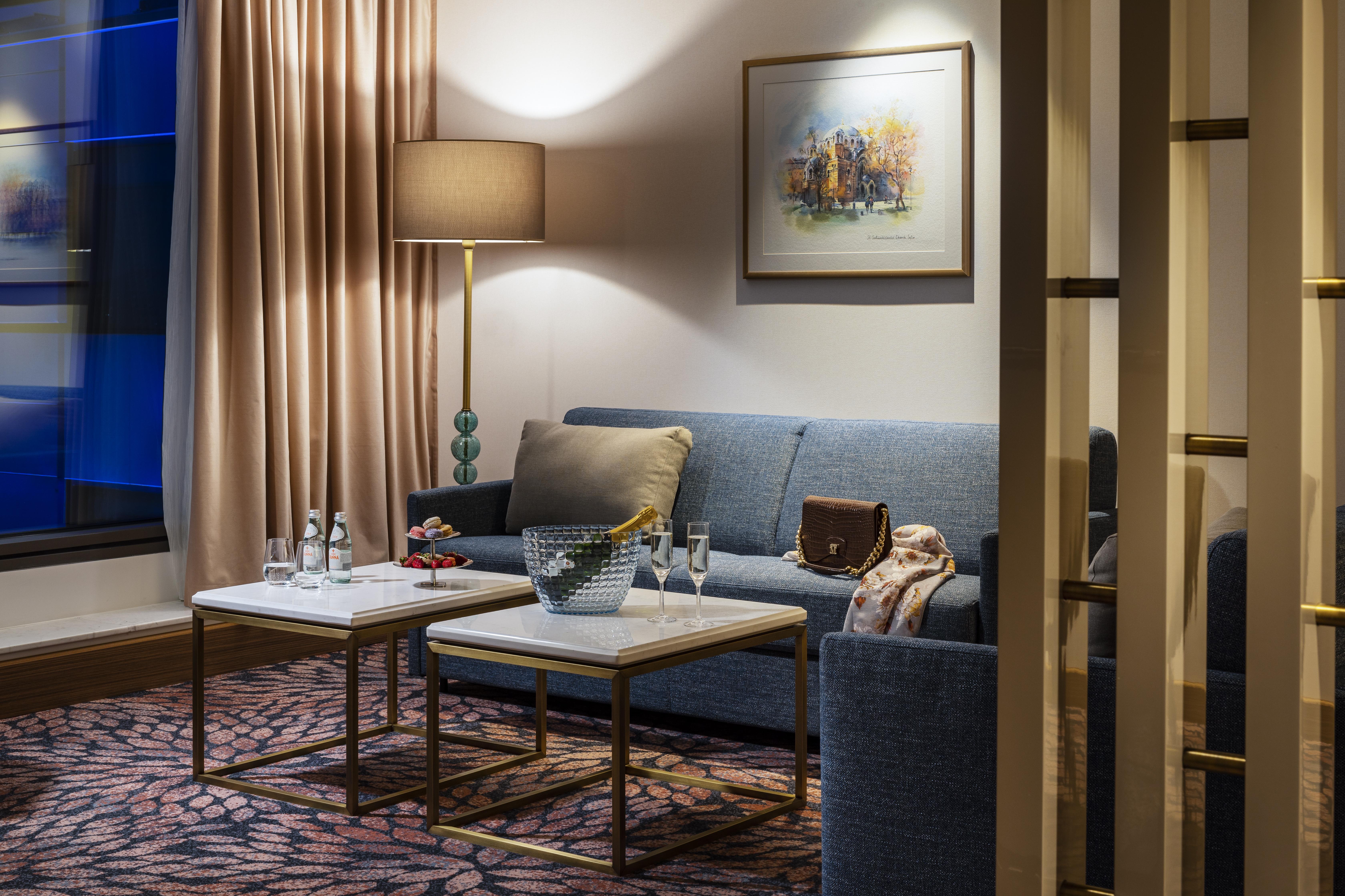 Grand Hotel Millennium โซเฟีย ภายนอก รูปภาพ The photo shows a cozy and elegantly decorated living space. It features a blue sofa against a wall, complemented by a painting above it. There are two small marble-top coffee tables with gold frames, one of which holds decorative items and glasses. 