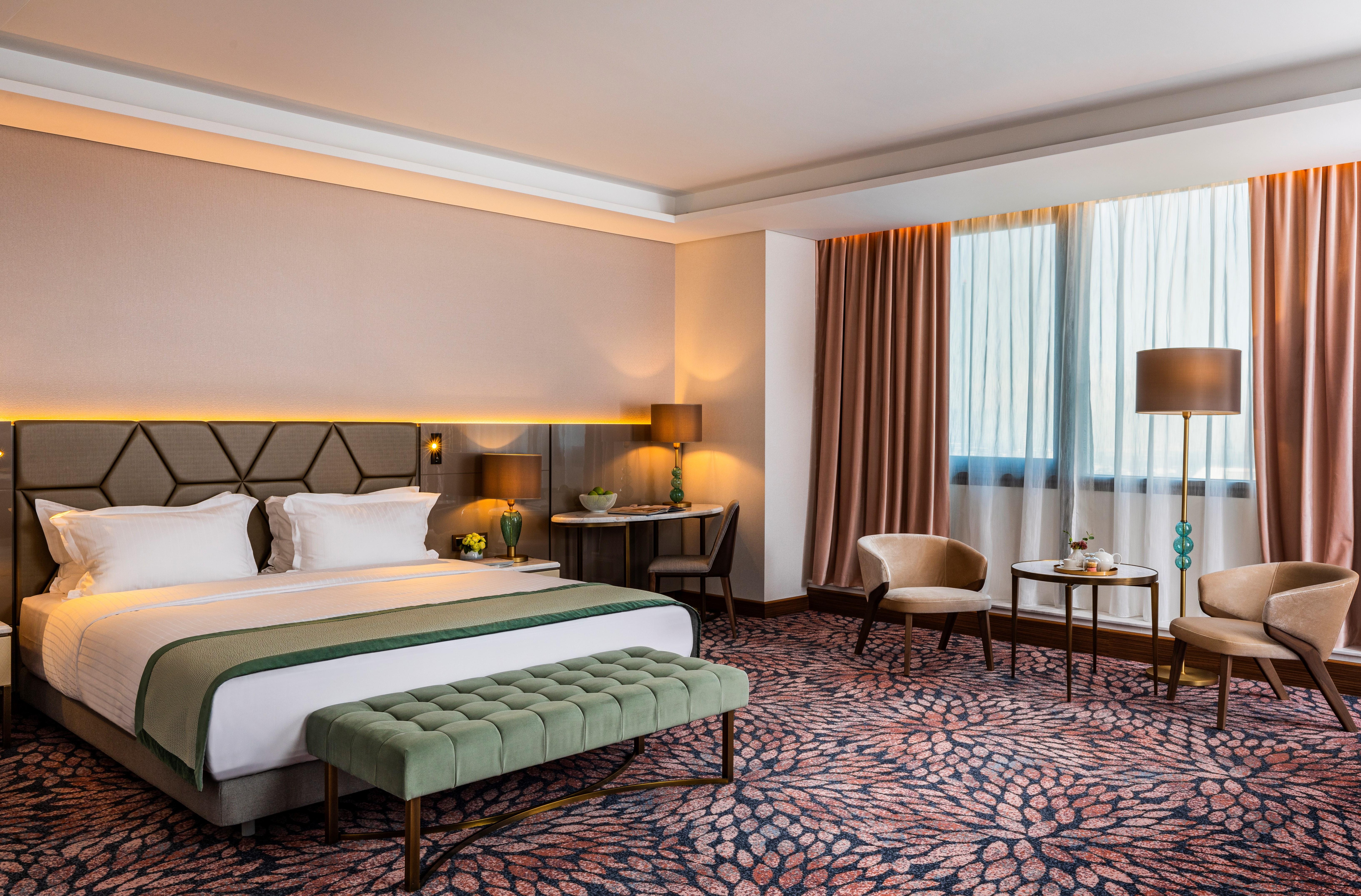 Grand Hotel Millennium โซเฟีย ภายนอก รูปภาพ The photo shows a modern hotel room. It features a large bed with a headboard, topped with two white pillows and a green throw blanket. In front of the bed, there is a stylish green bench. On either side of the bed, there are bedside tables with lamp
