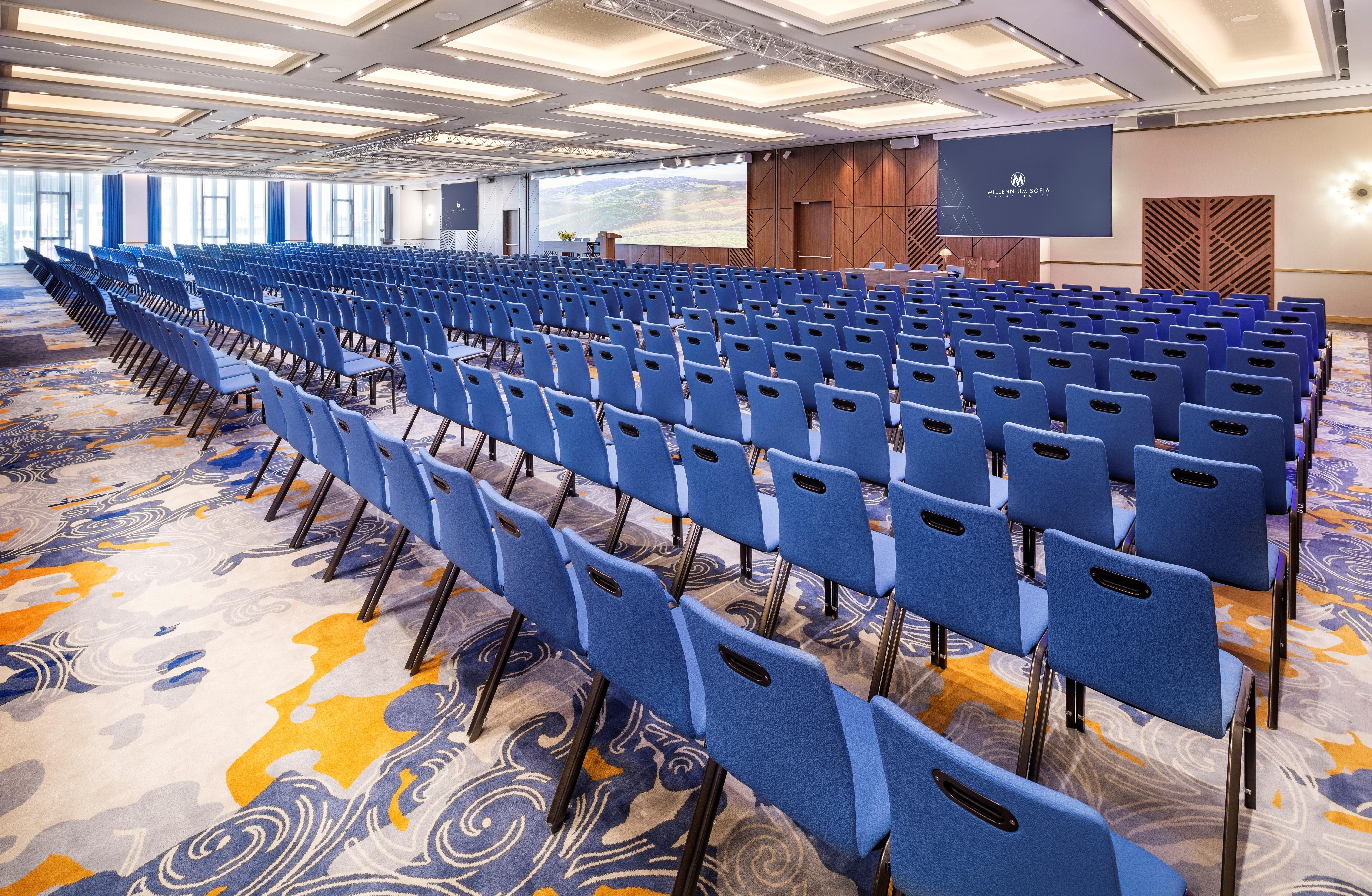 Grand Hotel Millennium โซเฟีย ภายนอก รูปภาพ The photo shows a large conference or meeting room set up for an event. There are numerous blue chairs arranged in rows, creating a seating area for attendees. The floor features a decorative pattern, and the room has a modern design with ample light
