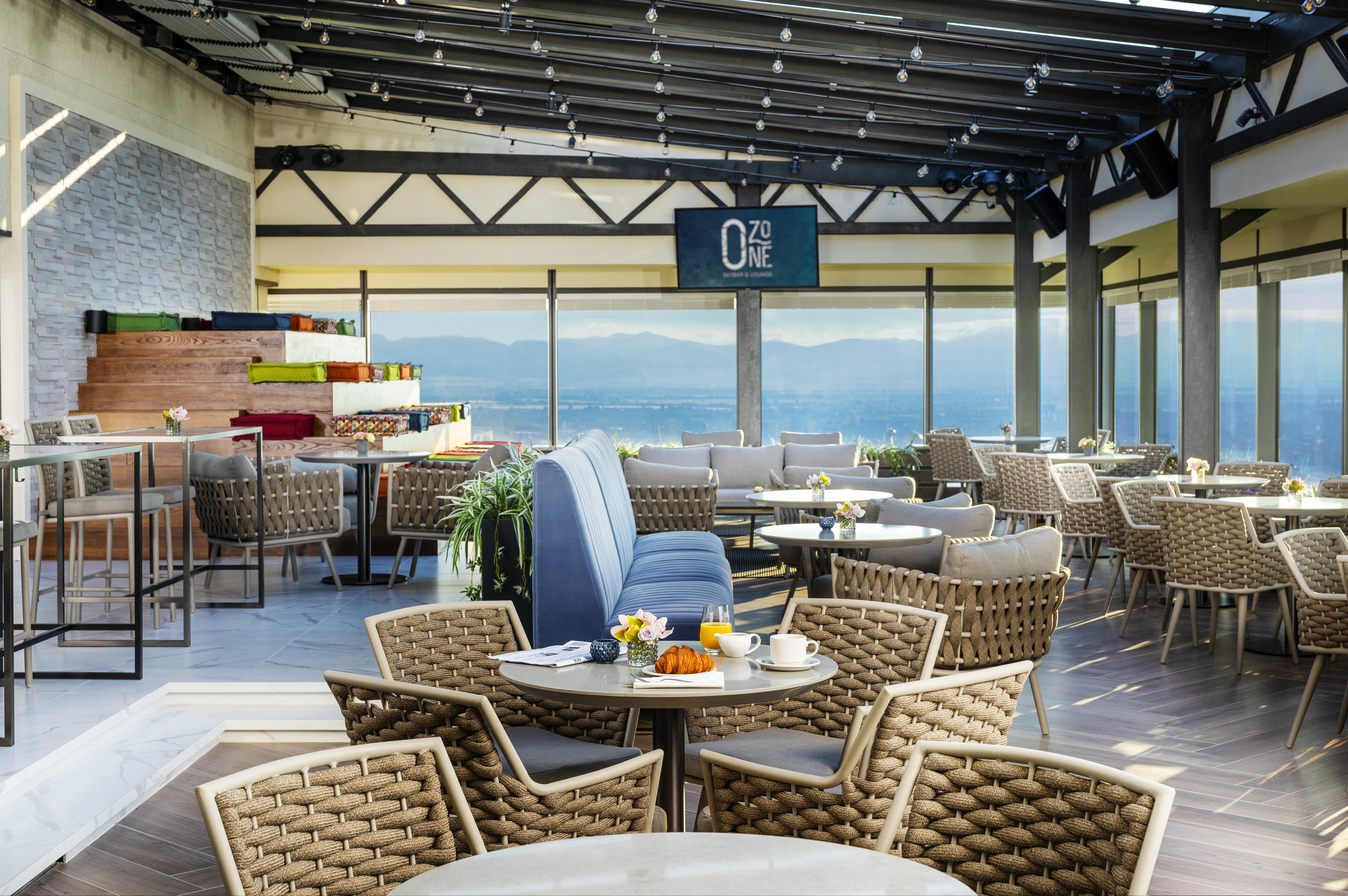 Grand Hotel Millennium โซเฟีย ภายนอก รูปภาพ The photo shows a modern restaurant or café with a spacious interior. It features a variety of seating arrangements, including round tables surrounded by wicker chairs and lounges. Large windows allow for a panoramic view, which likely includes sceni